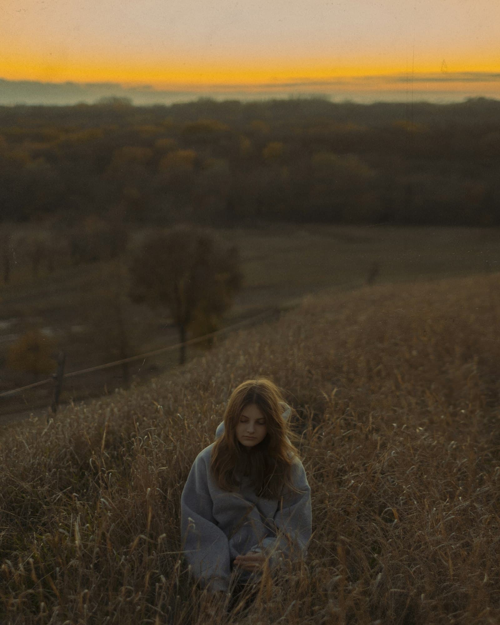 A woman sitting quietly in a field at dusk
